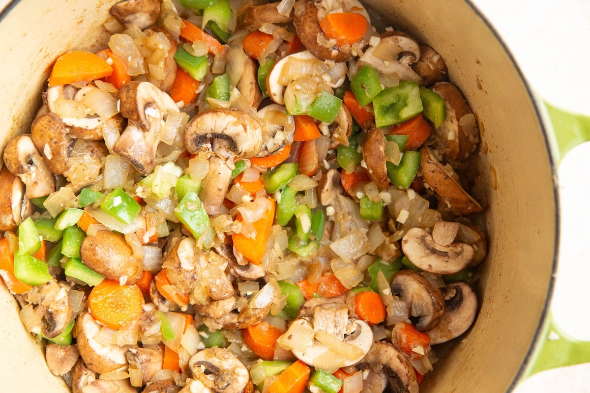 Mushrooms, bell pepper, carrots, garlic and onions sautéing in a pot.