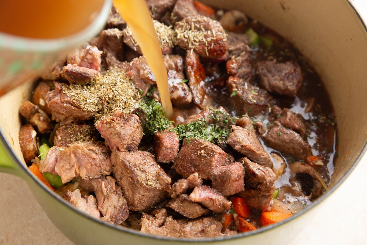 Pouring beef broth into the pot with the stew meat.