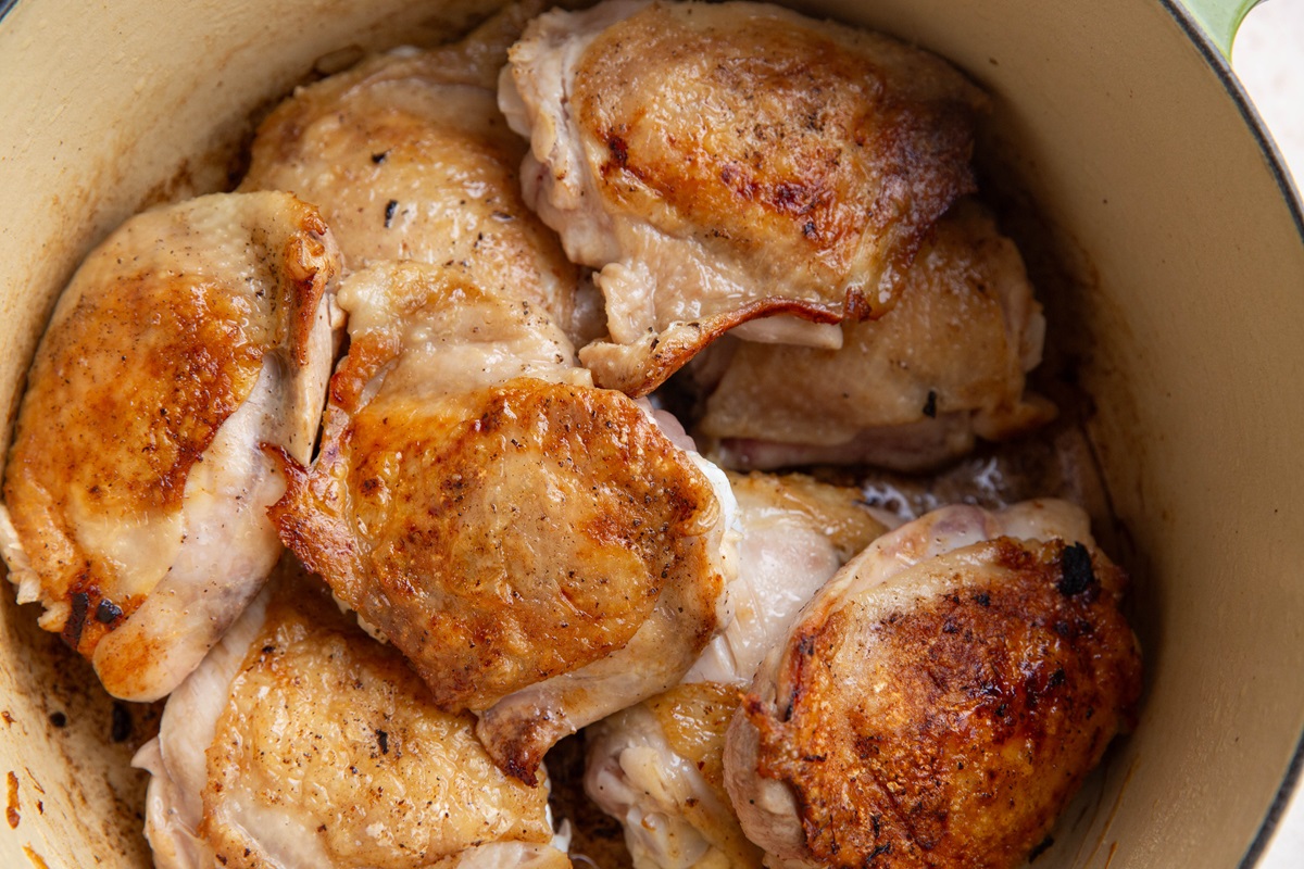 Pile of browned chicken thighs in a Dutch oven.