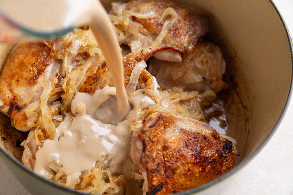 Pouring liquid into a Dutch oven with chicken.