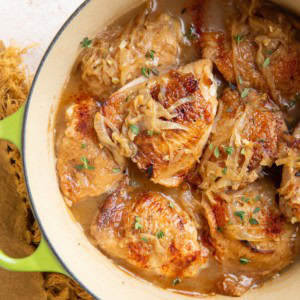 Dutch oven full of chicken thighs with a cream sauce. Golden napkin and fresh thyme to the side.