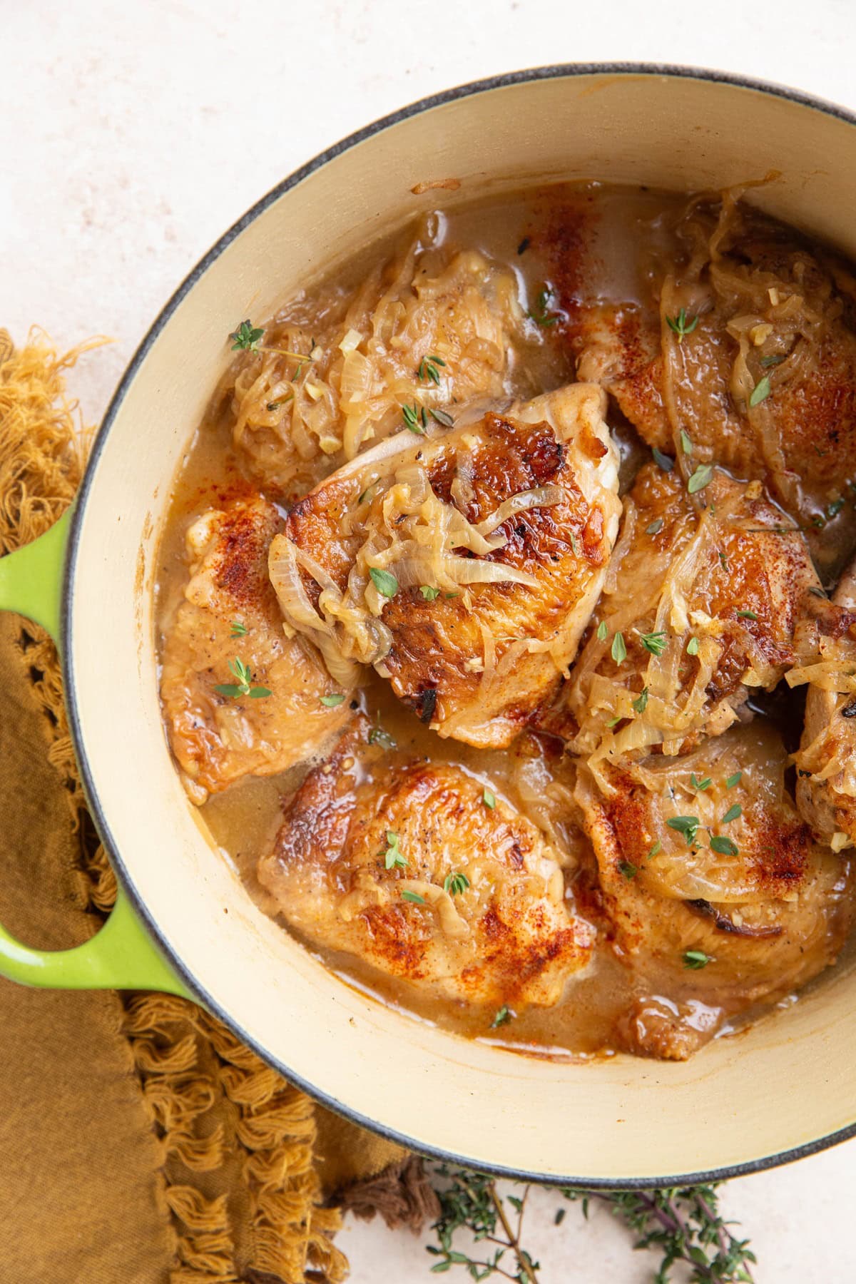 Dutch oven full of chicken thighs with a cream sauce. Golden napkin and fresh thyme to the side.