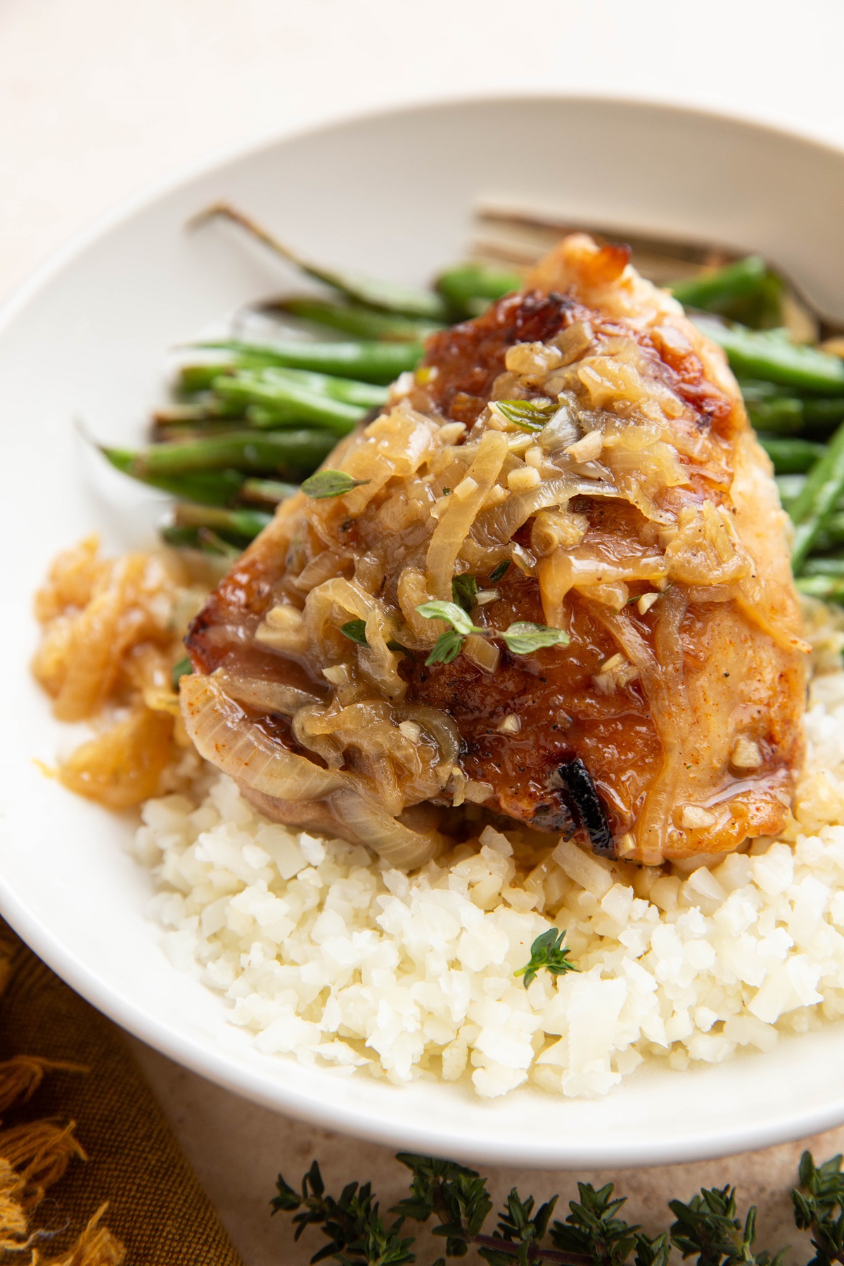 Chicken thigh with caramelized onions on top with cauliflower rice and green beans in a bowl, ready to eat.