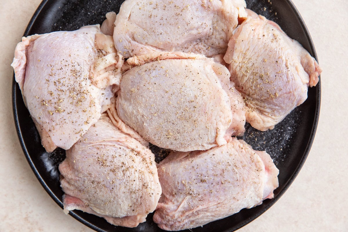 Chicken thighs on a plate sprinkled with salt and pepper.