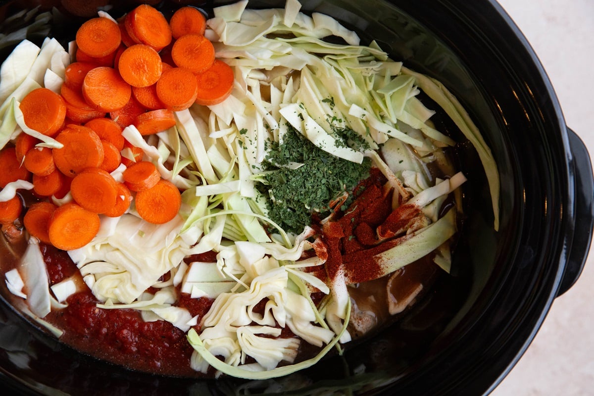Crock pot with sausage, onion, broth, crushed tomatoes, cabbage, carrots, and seasonings.