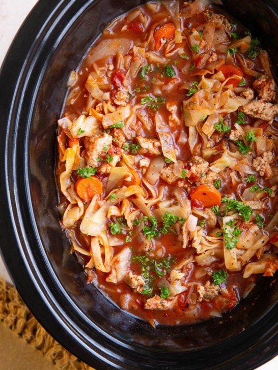 Slow Cooker full of sausage and cabbage soup. Garnished with parsley and ready to serve.
