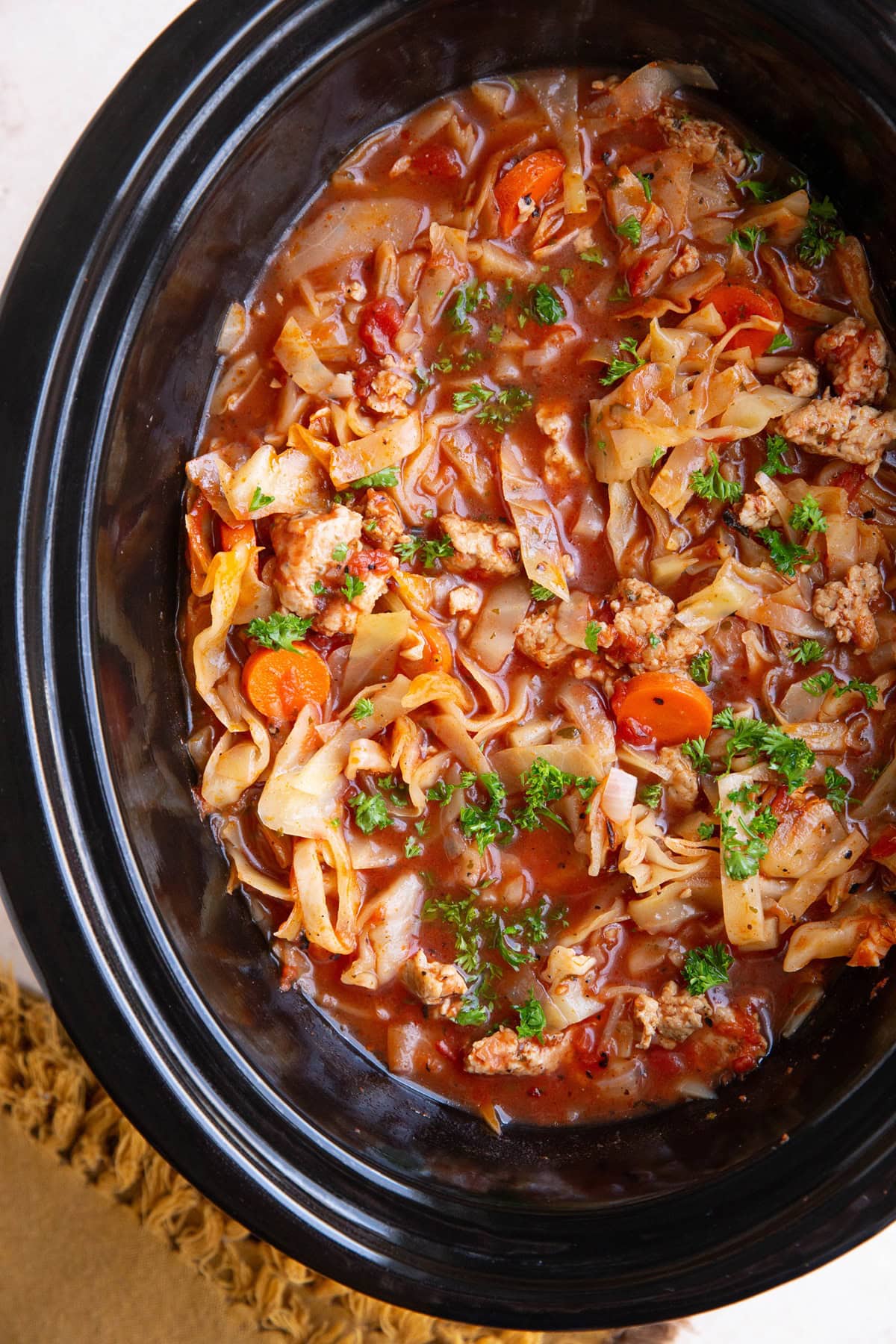 Slow Cooker full of sausage and cabbage soup. Garnished with parsley and ready to serve.