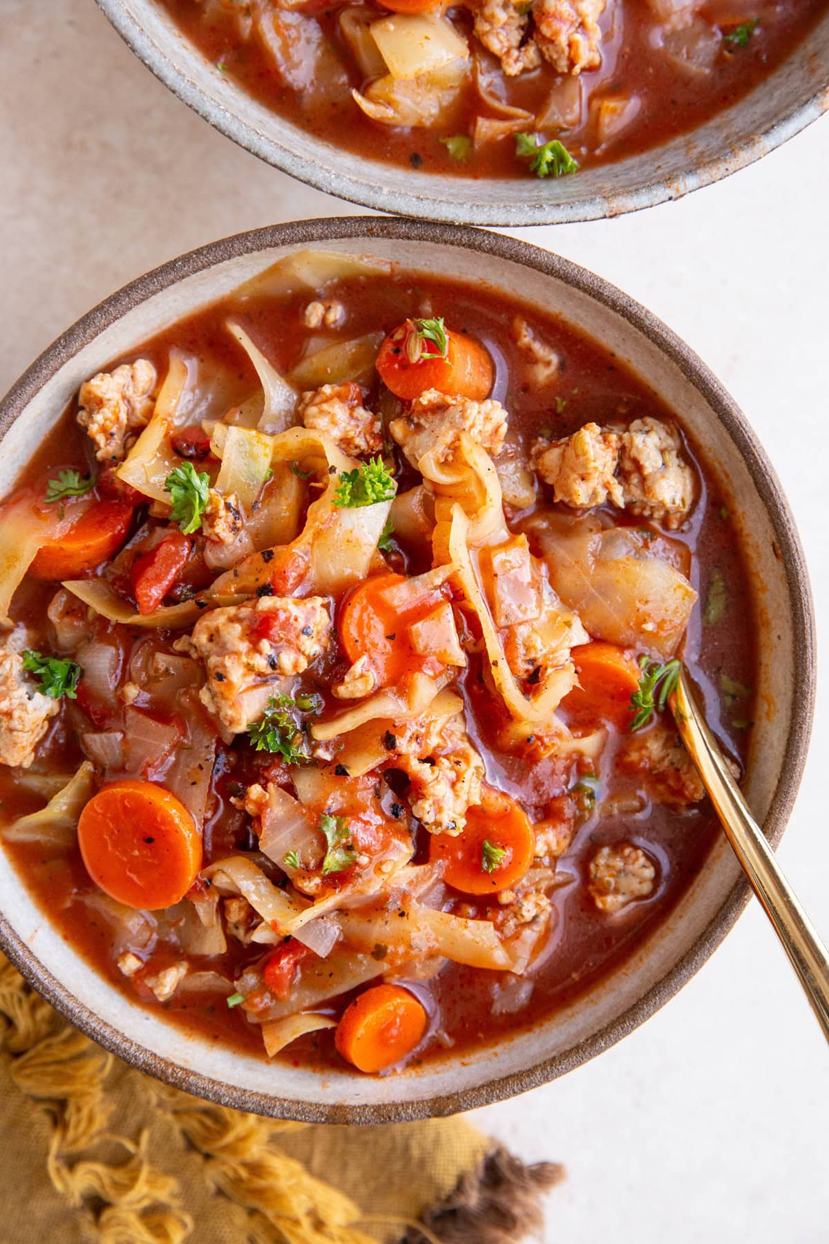 Two bowls of sausage and cabbage soup with a gold spoon and golden napkin. Ready to eat.