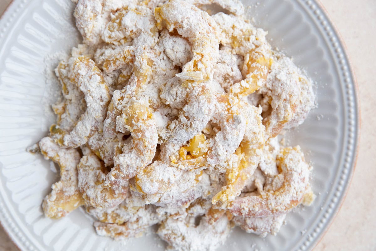 Shrimp doused with flour mixture on a plate, ready to cook.