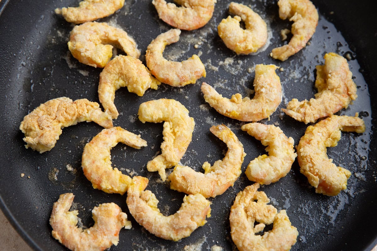 Large skillet with breaded shrimp cooking in it.