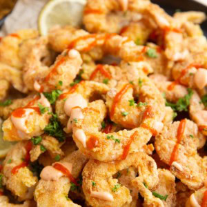 Crispy shrimp on a plate drizzled with sauce and fresh parsley, ready to serve.