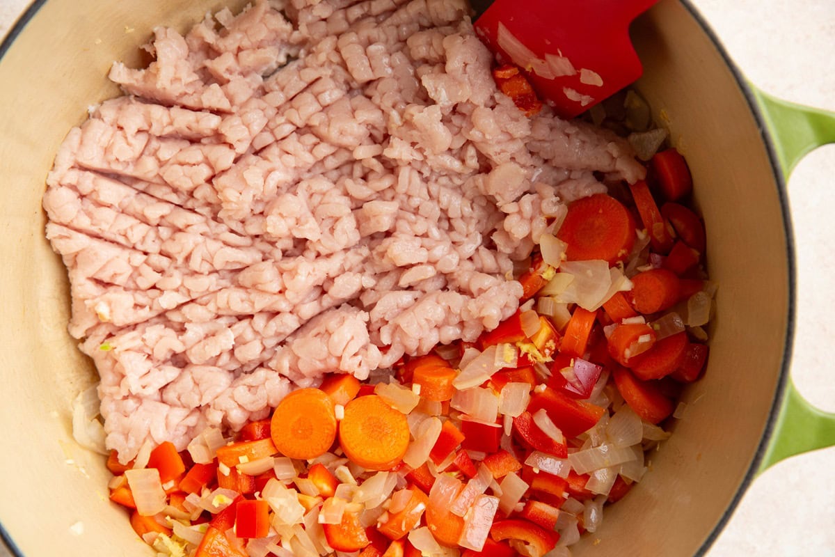 Ground turkey cooking on one side of a large pot with vegetables cooking on the other side of a large pot.