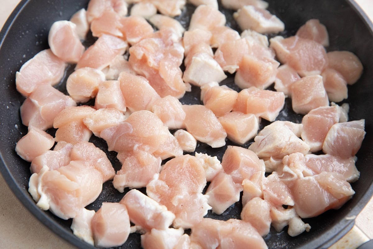 Raw chicken pieces in a skillet, browning.