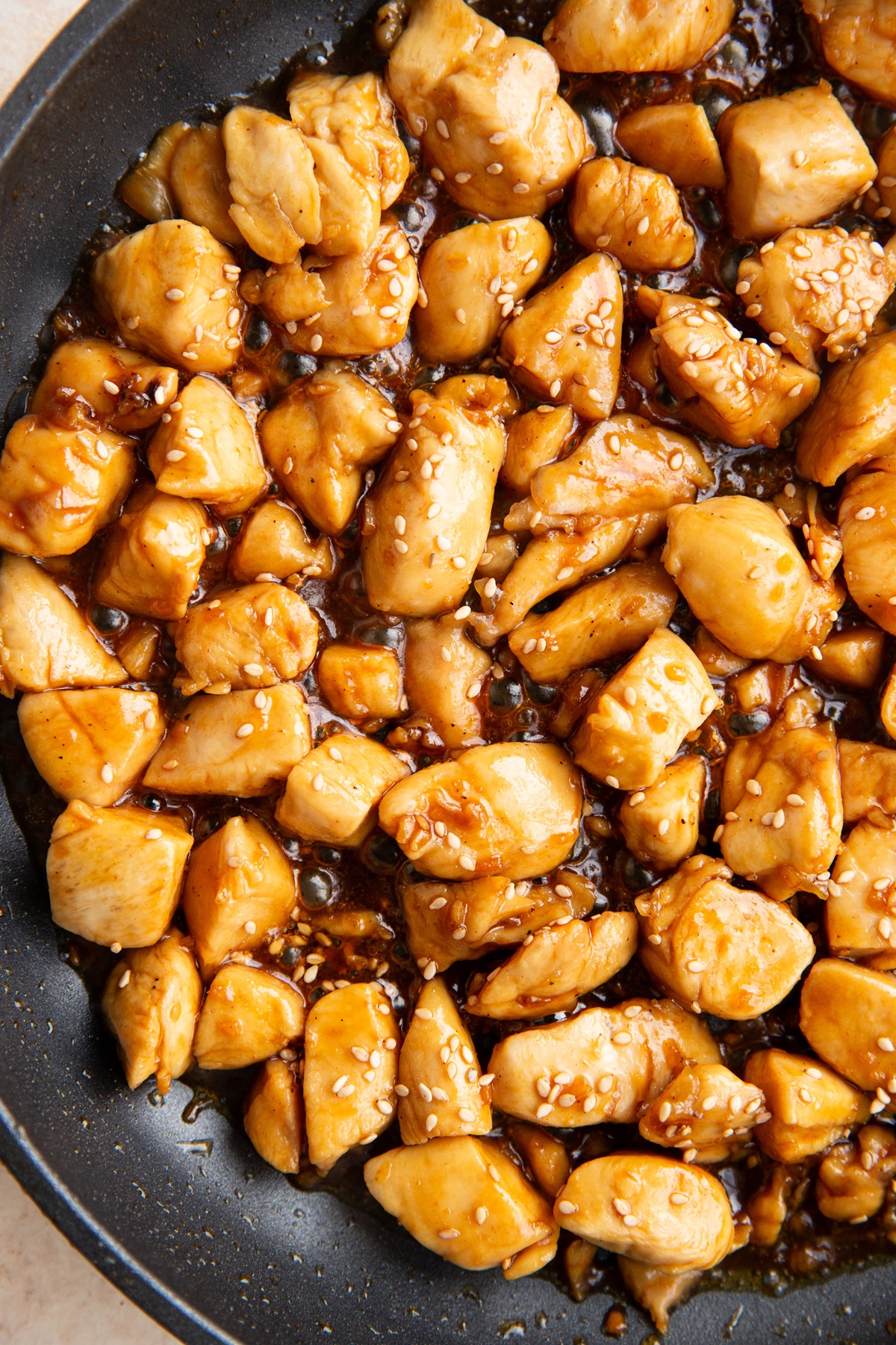 Sesame chicken in a skillet, sprinkled with sesame seeds and ready to eat.