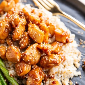 Plate of brown rice, sesame chicken, and asparagus, ready to eat.