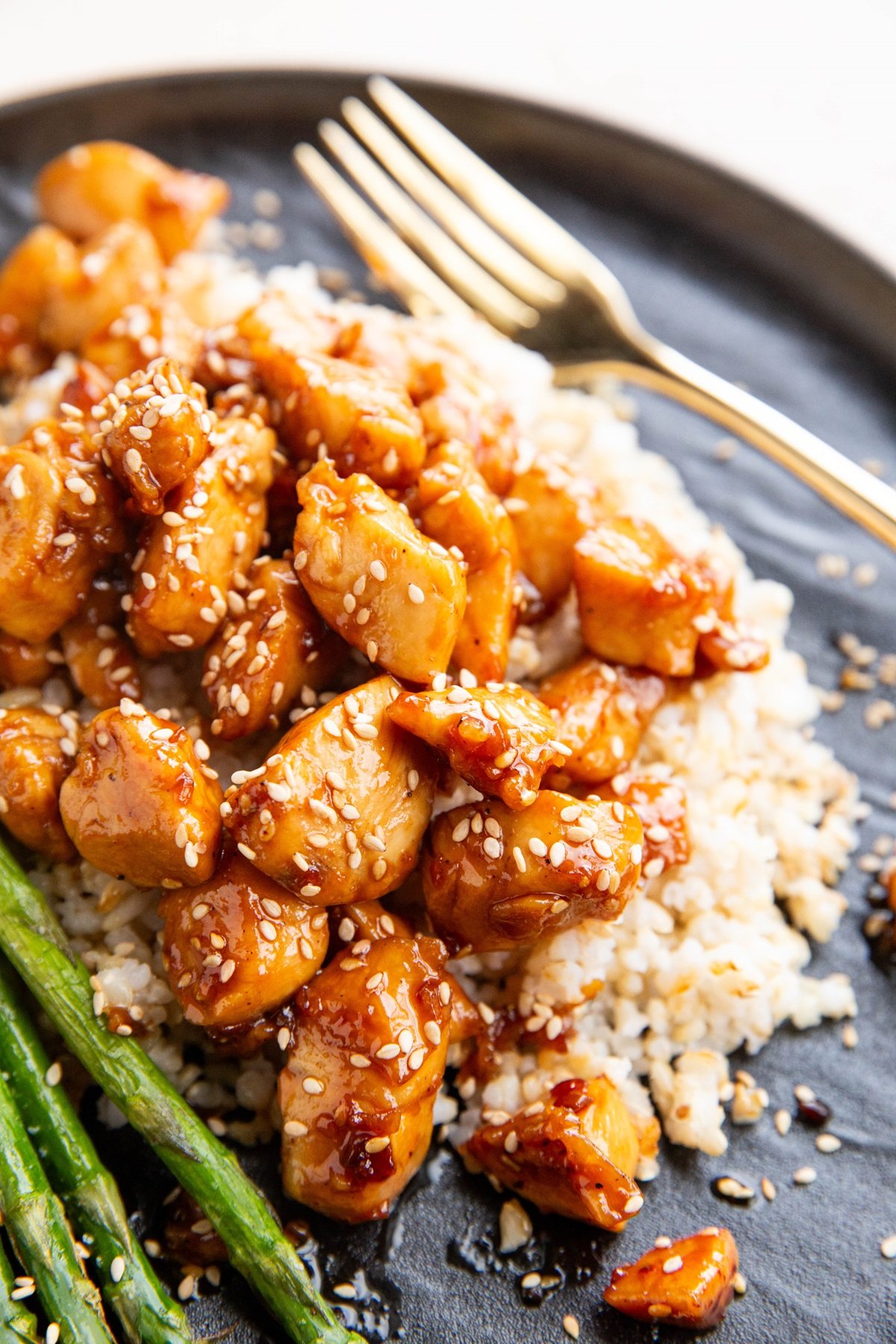 Plate of brown rice, sesame chicken, and asparagus, ready to eat.