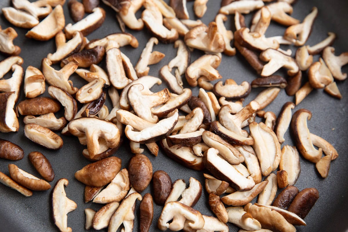 Shiitake mushrooms cooking in a skillet.