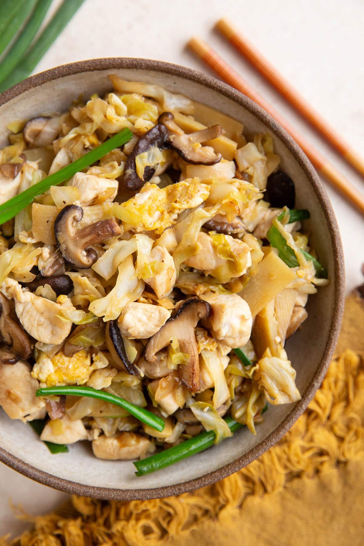 Bowl of moo shu chicken with chop sticks to the side and a napkin next to the bowl..