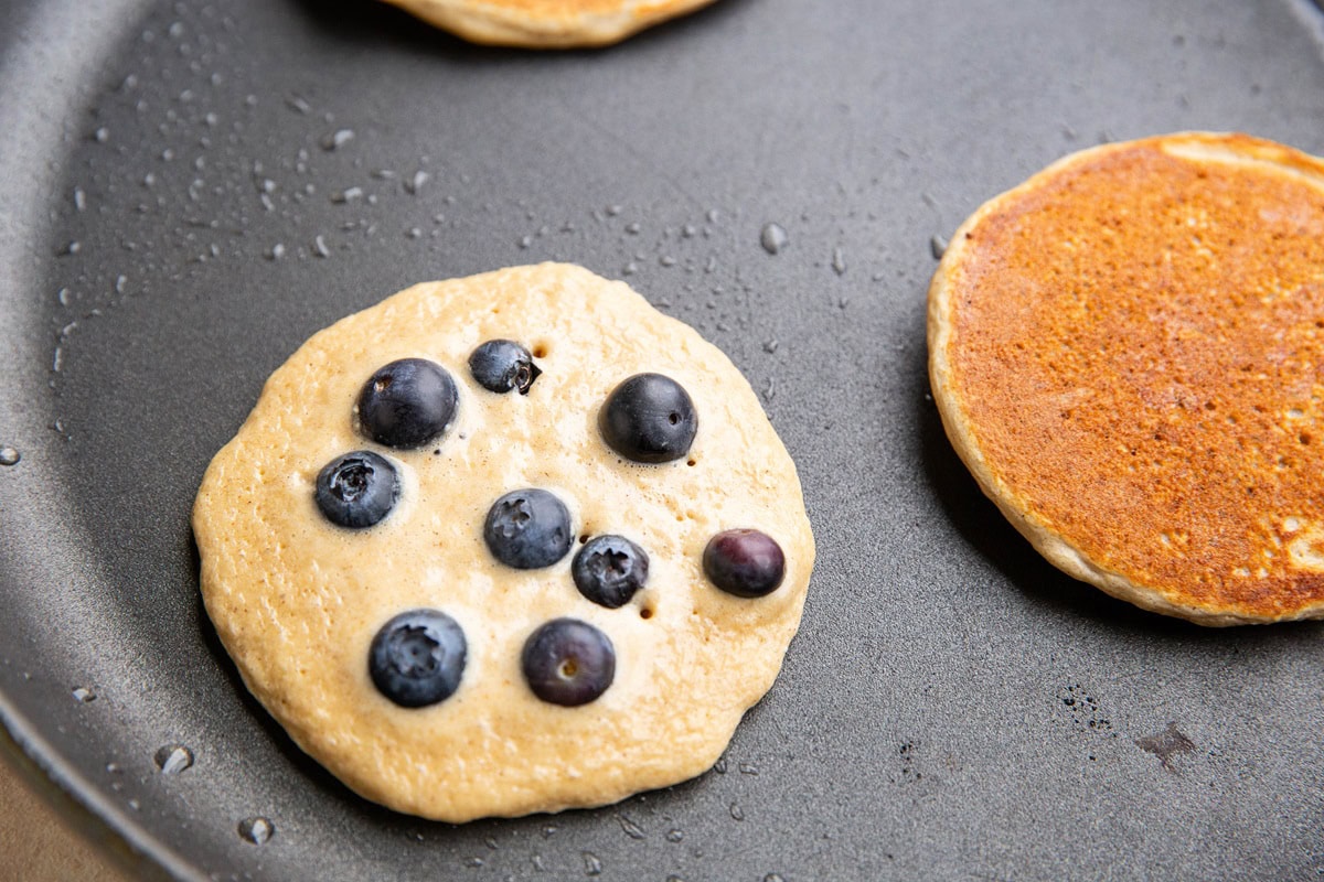 Blueberry pancakes cooking on a skillet.