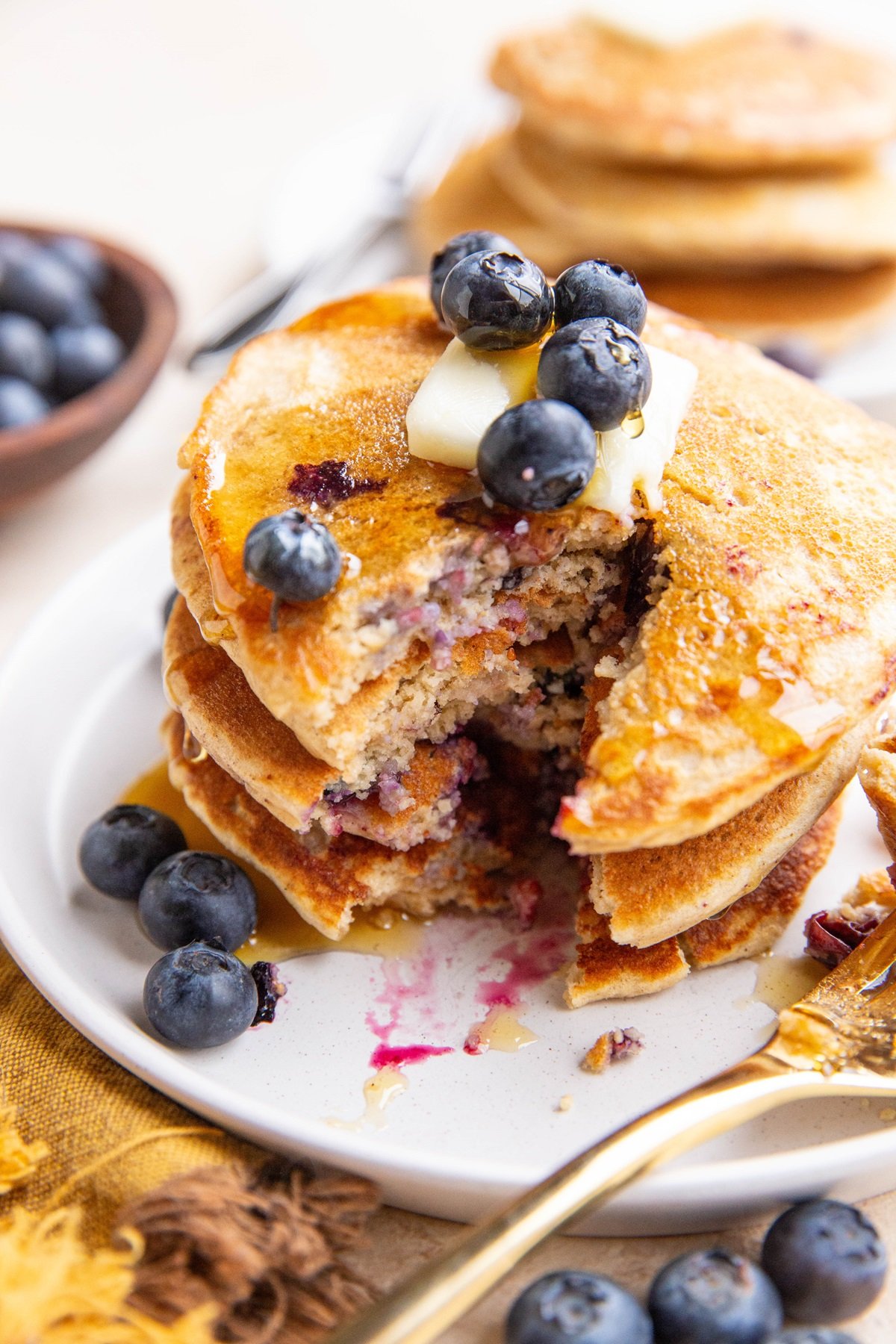 Stack of oatmeal pancakes on a plate with butter and blueberries on top and a bite taken out.