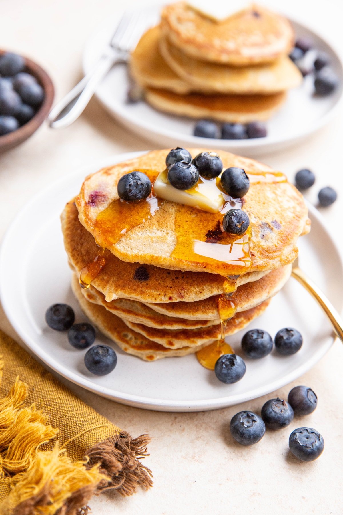 Stack of oatmeal blueberry pancakes on a white plate, drizzled with honey and topped with butter and fresh berries.