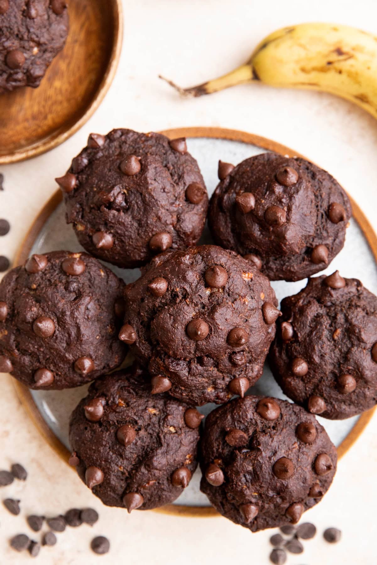 Plate of oatmeal chocolate banana muffins with a ripe banana to the side and chocolate chips sprinkled all around.