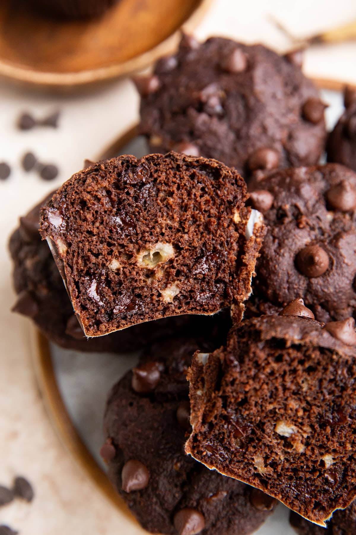 Plate of chocolate banana muffins with one muffin cut in half to you can see the melty chocolate chips on the inside.