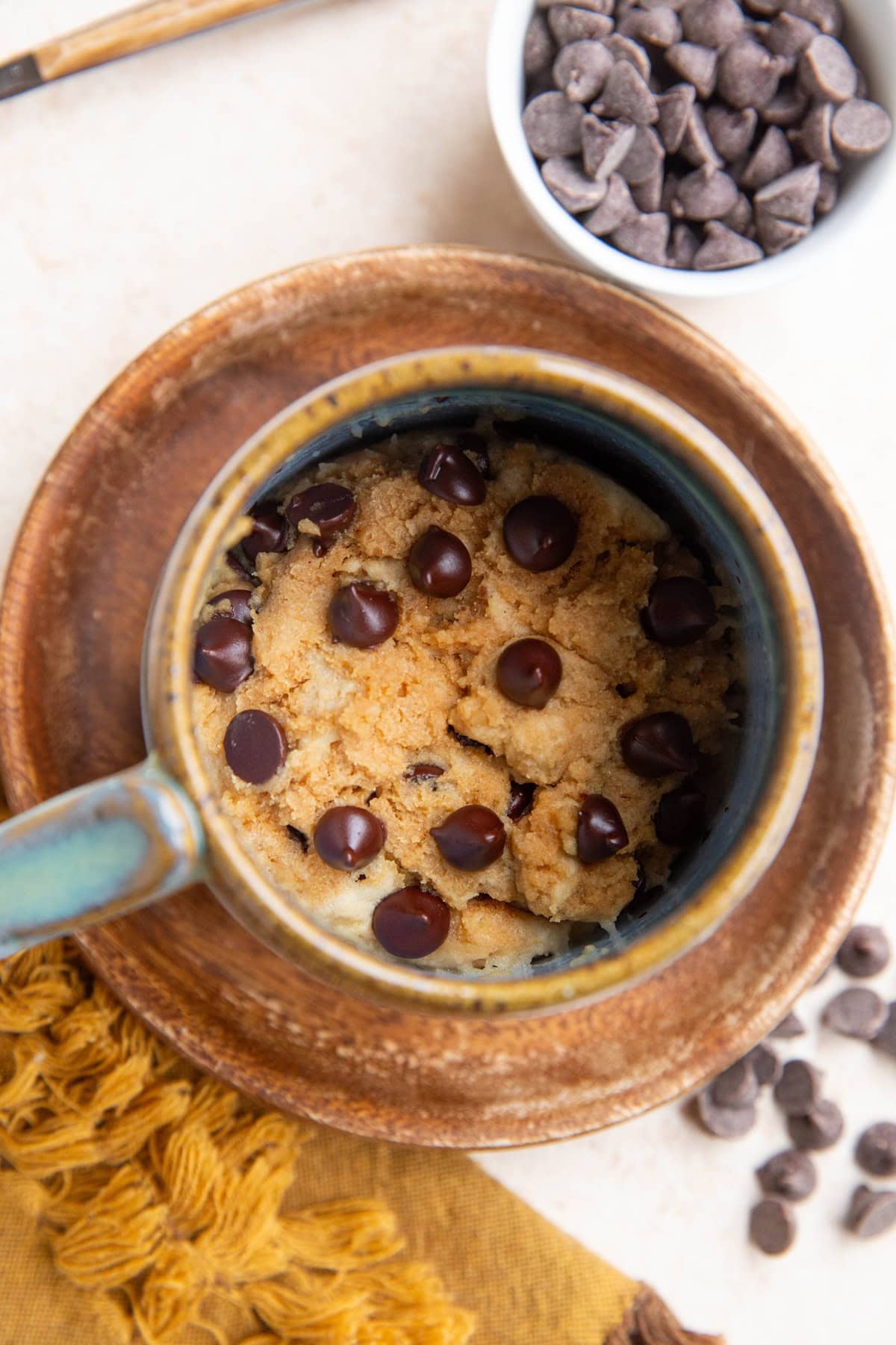 Peanut butter mug cake in a blue ceramic mug with a small bowl of chocolate chips and a napkin to the side.