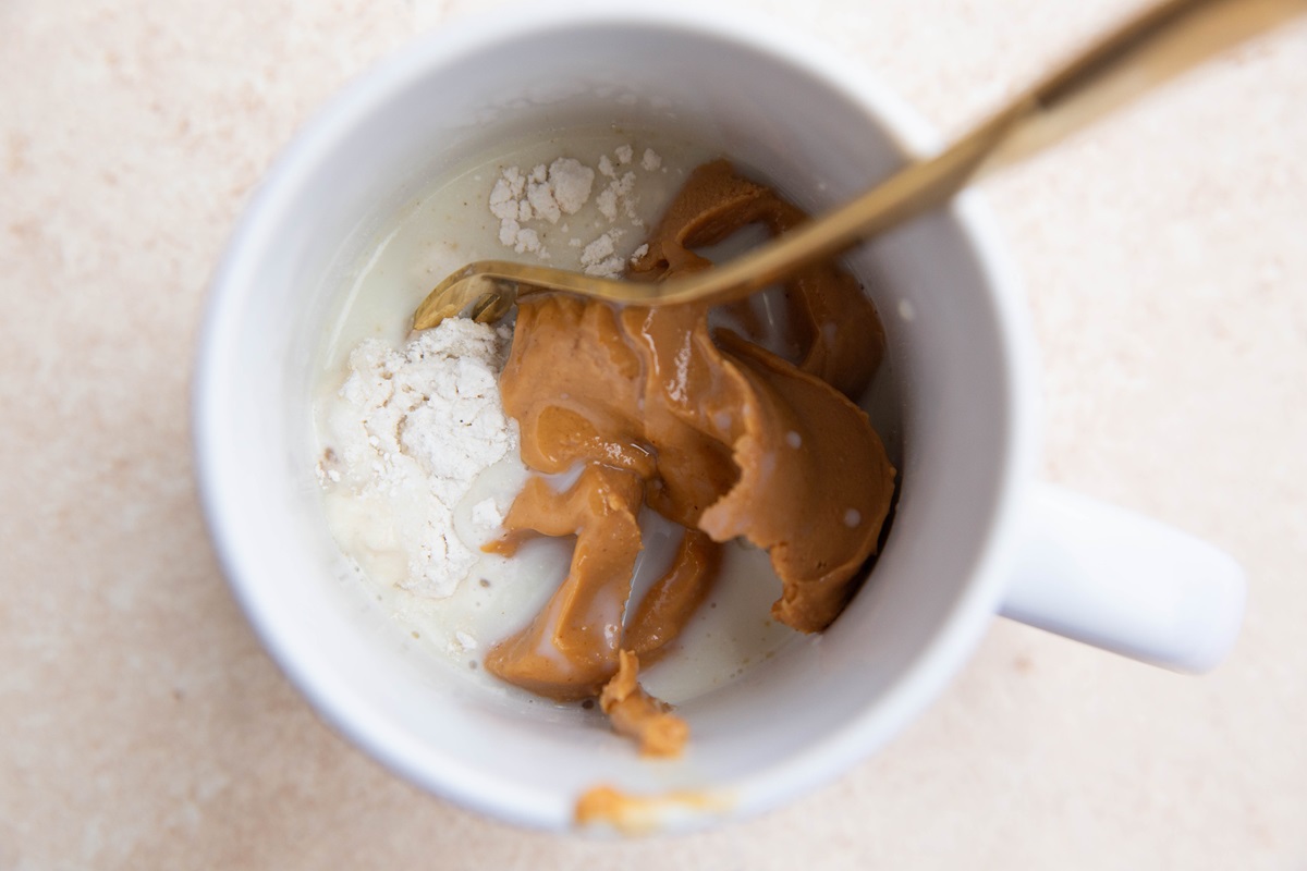 Mug with ingredients for peanut butter mug cake inside with a spoon to stir everything up.