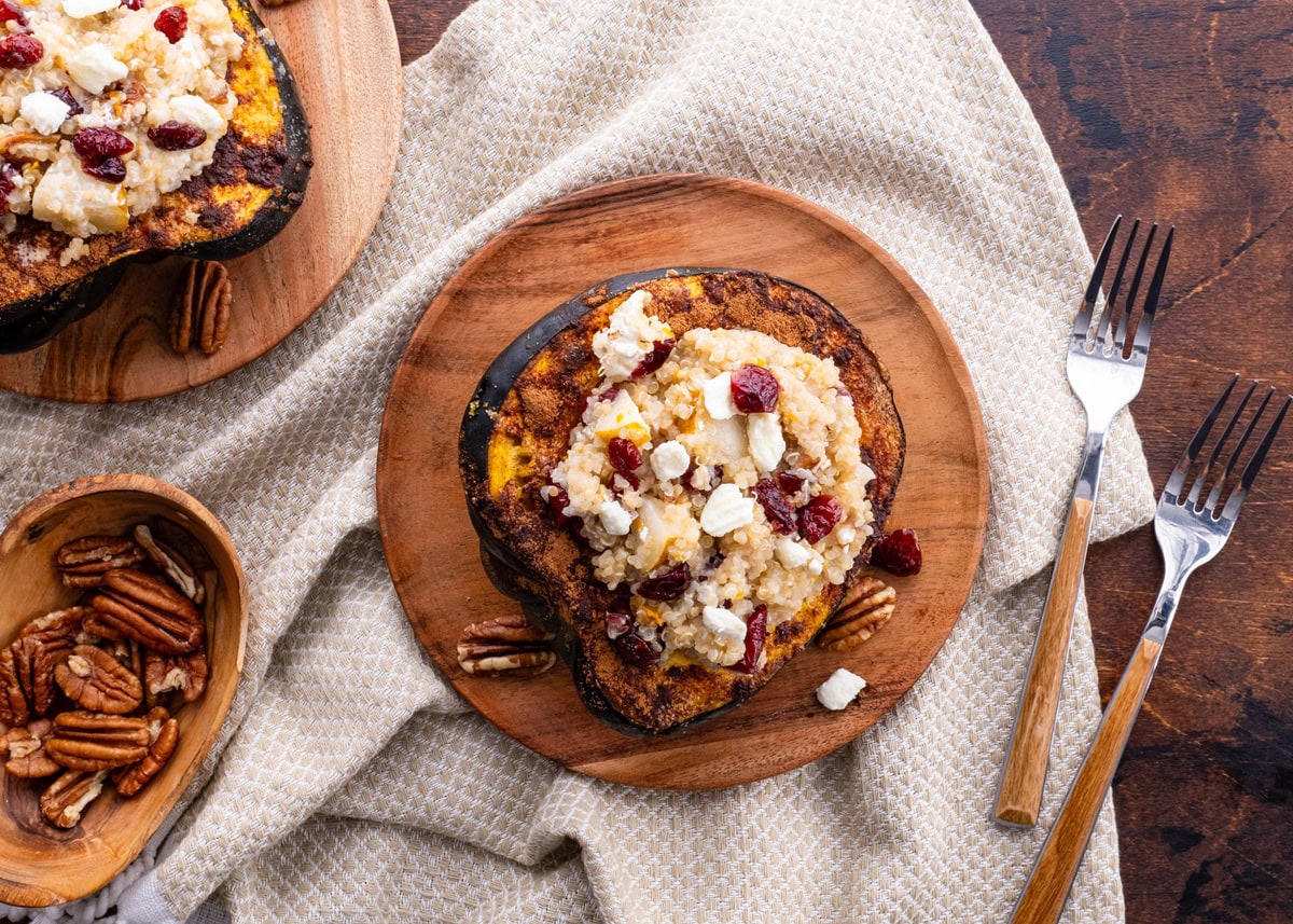 Two halves of acorn squash on two plates stuffed with quinoa mixture. Forks to the sides.