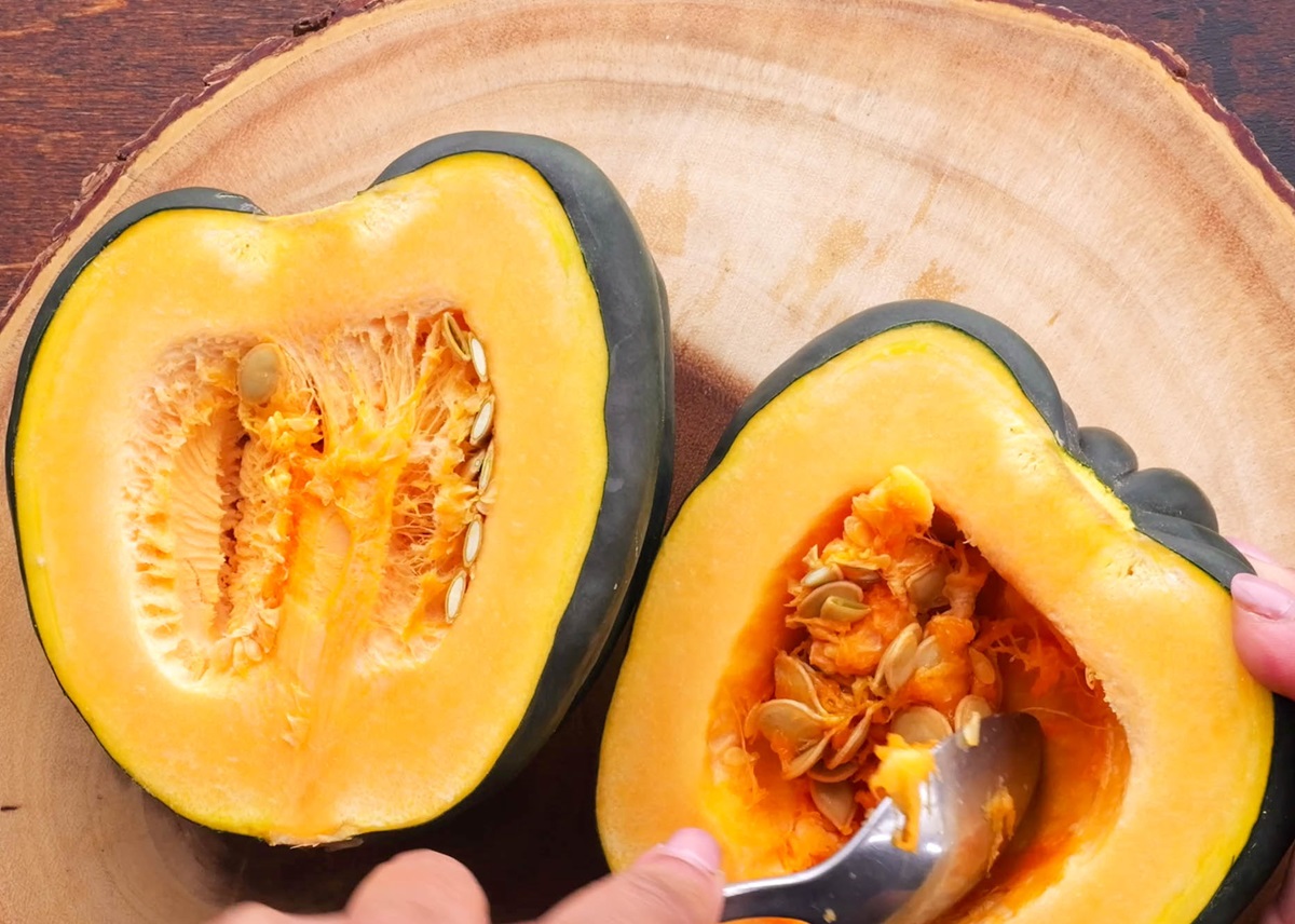 Hand scooping out the stringy bits and seeds from an acorn squash.