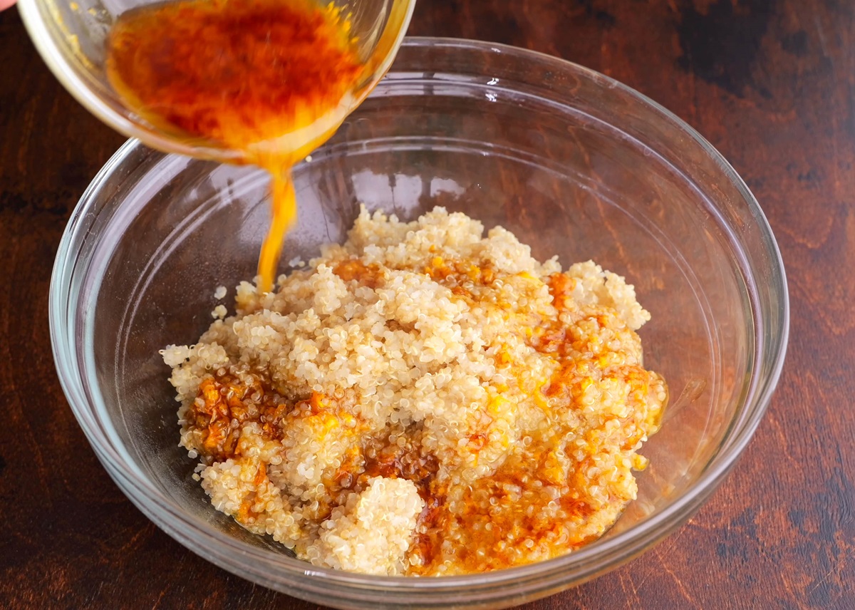Pouring orange dressing into the bowl with cooked quinoa.