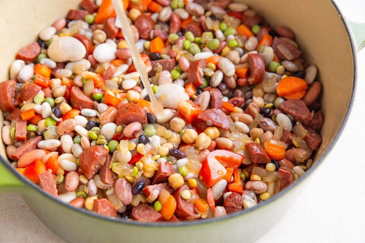Pouring broth into a pot of beans, vegetables and sausage.