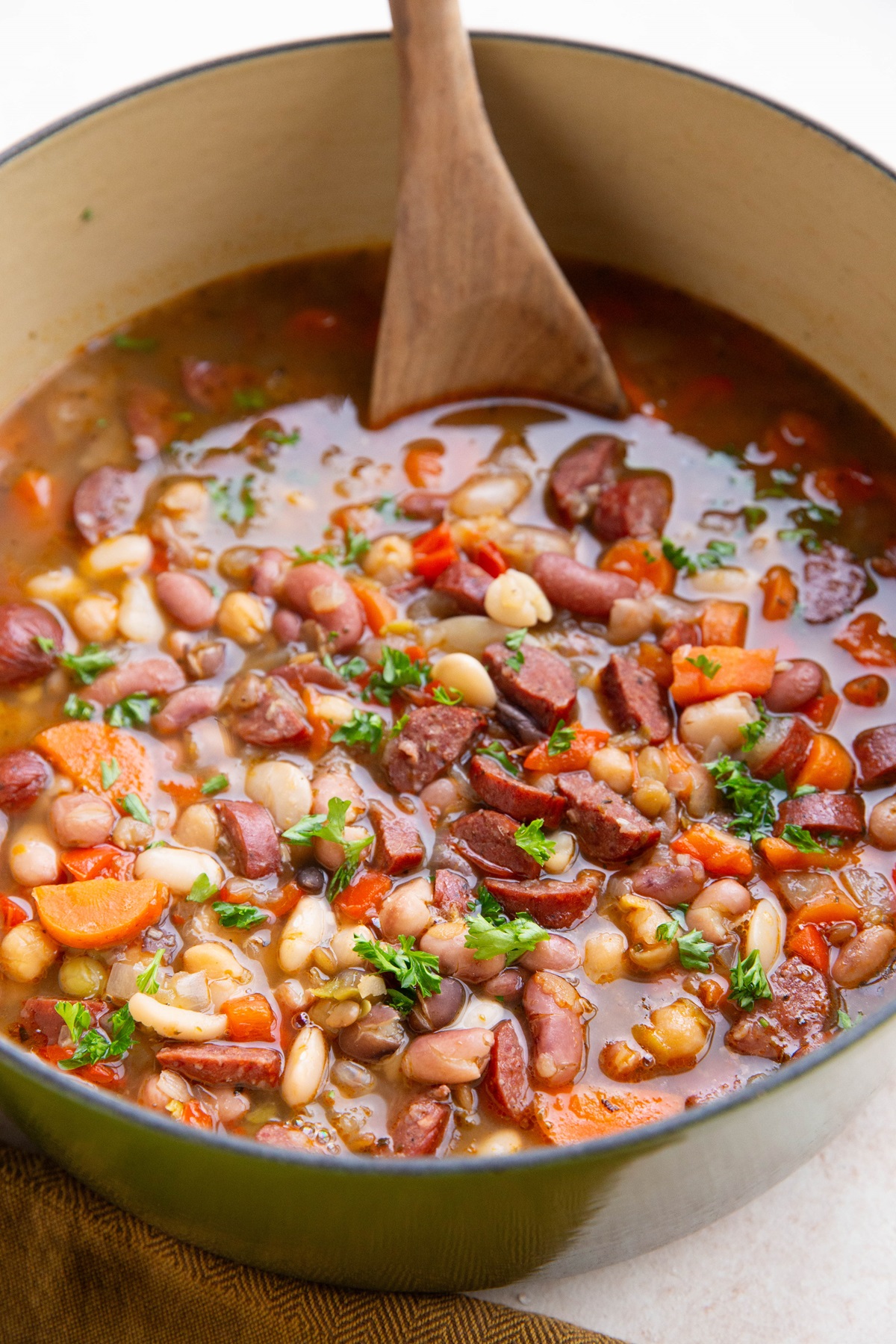 Sausage and bean soup in a large pot with a wooden spoon, ready to serve.