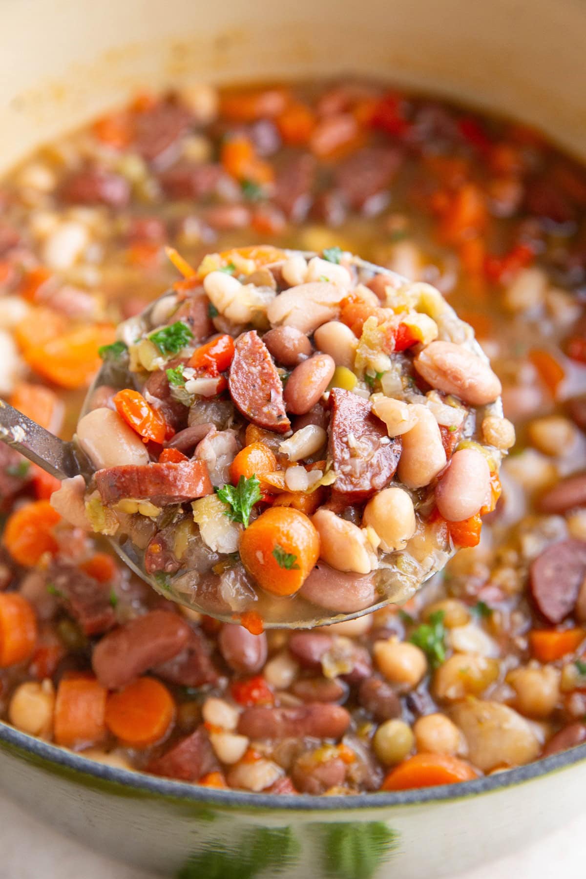 Ladle scooping a serving of sausage and bean soup out of a pot.