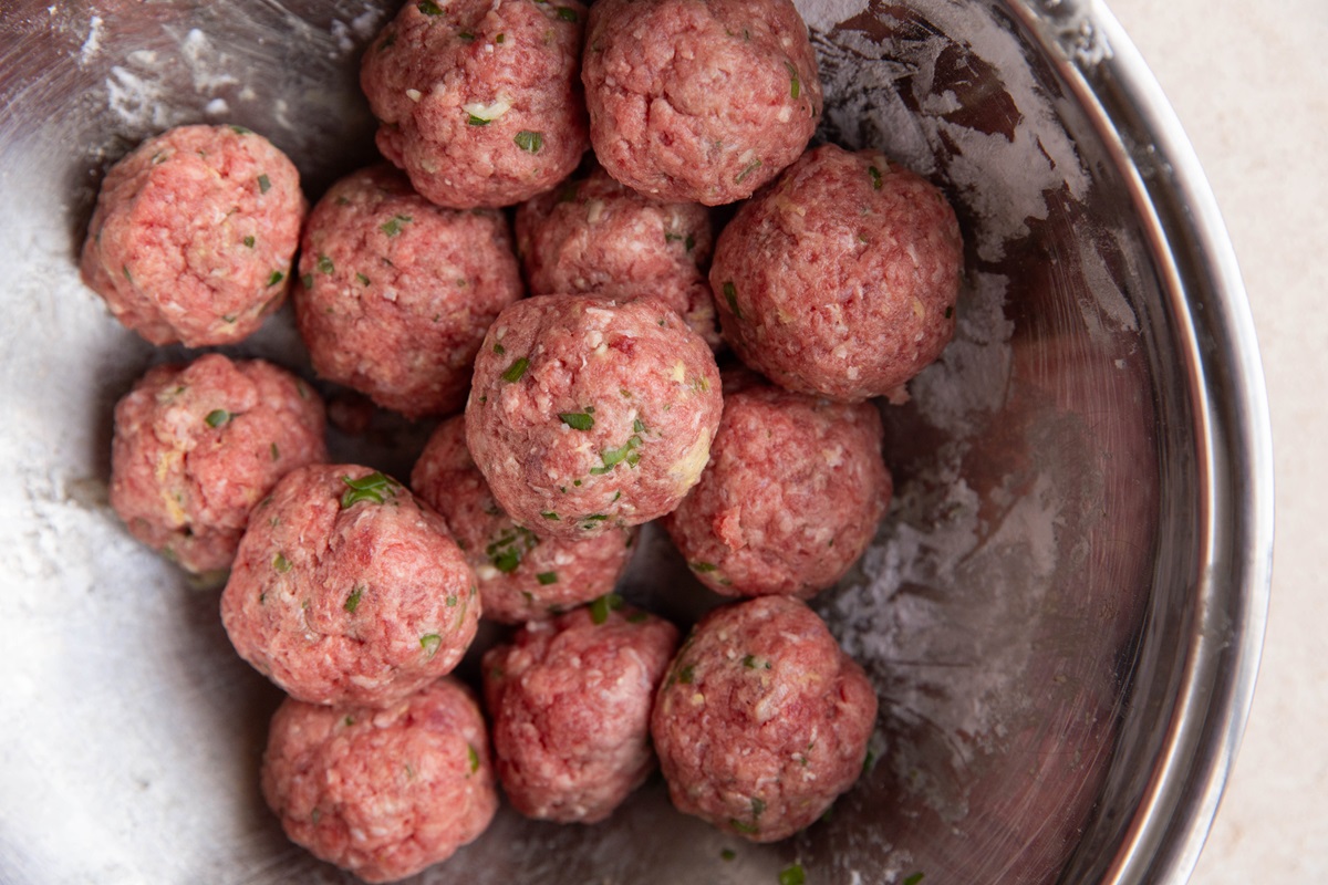 Stainless steel bowl full of raw meatballs, ready to be cooked.