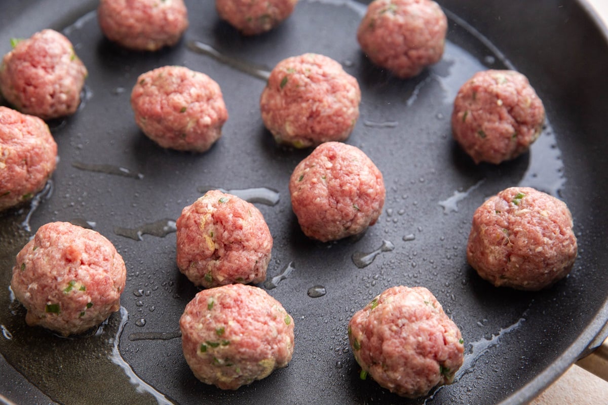 Meatballs cooking on a skillet in oil.