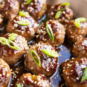 Stainless steel skillet full of glazed meatballs with green onions and sesame seeds on top.