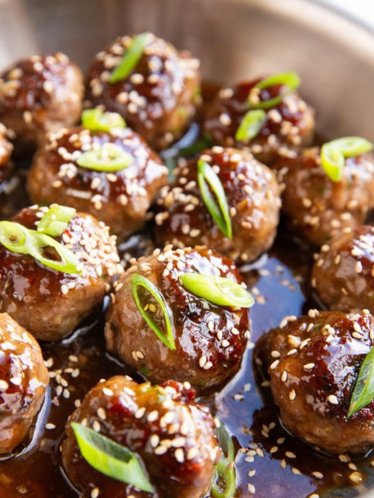 Stainless steel skillet full of glazed meatballs with green onions and sesame seeds on top.