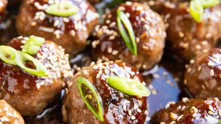 Stainless steel skillet full of glazed meatballs with green onions and sesame seeds on top.