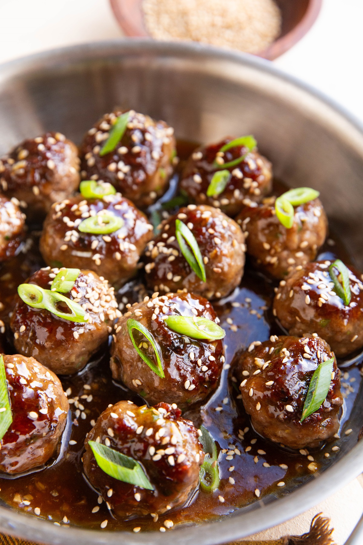 Garlic sesame meatballs in a skillet in a sticky sauce. Sprinkled with green onions and plenty of sesame seeds.