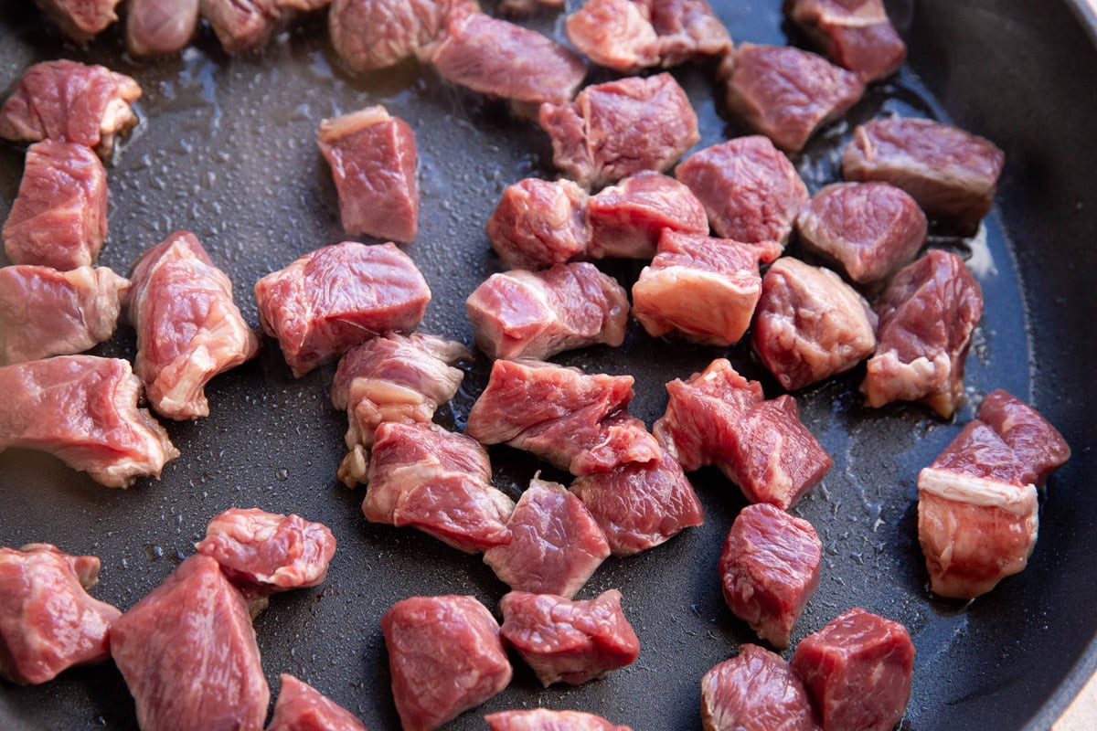 Raw bites of steak in a skillet browning.