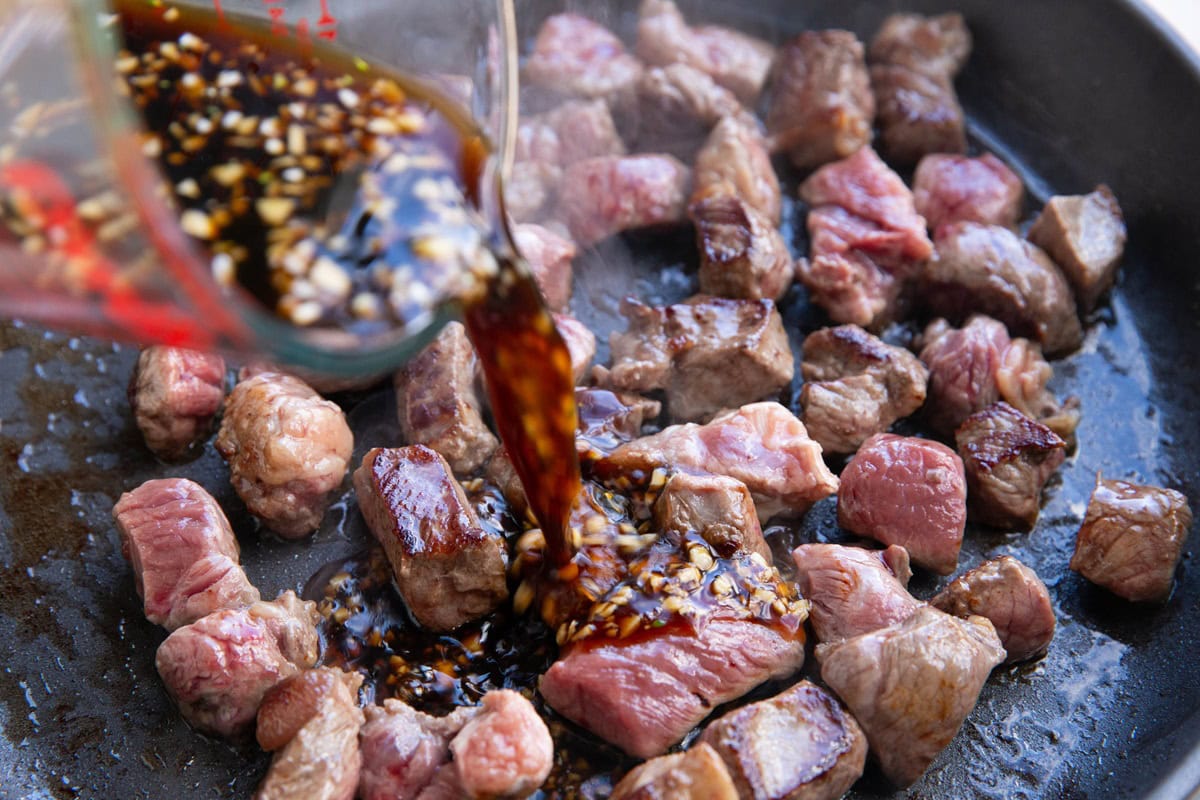 Pouring sauce mixture in a skillet to make Asian steak bites.