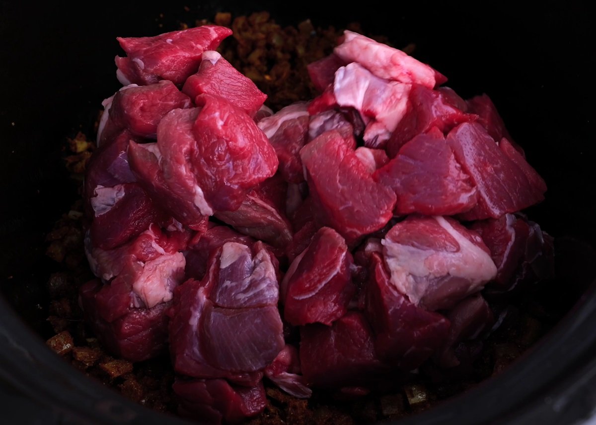Lamb stew meat in a crock pot with sauteed onion.