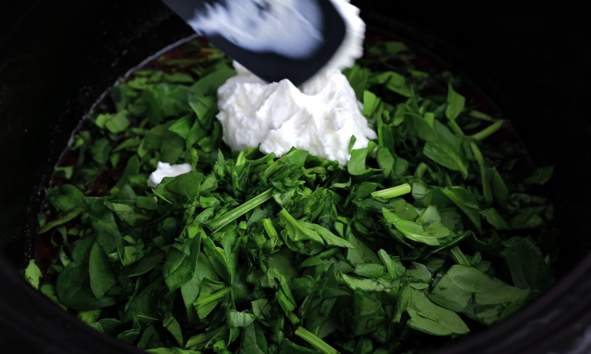 Baby spinach and Greek yogurt being added to the crock pot.