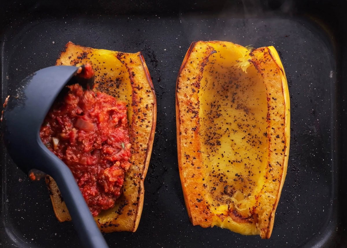 Ladle pouring sauce into the center of the spaghetti squash half.