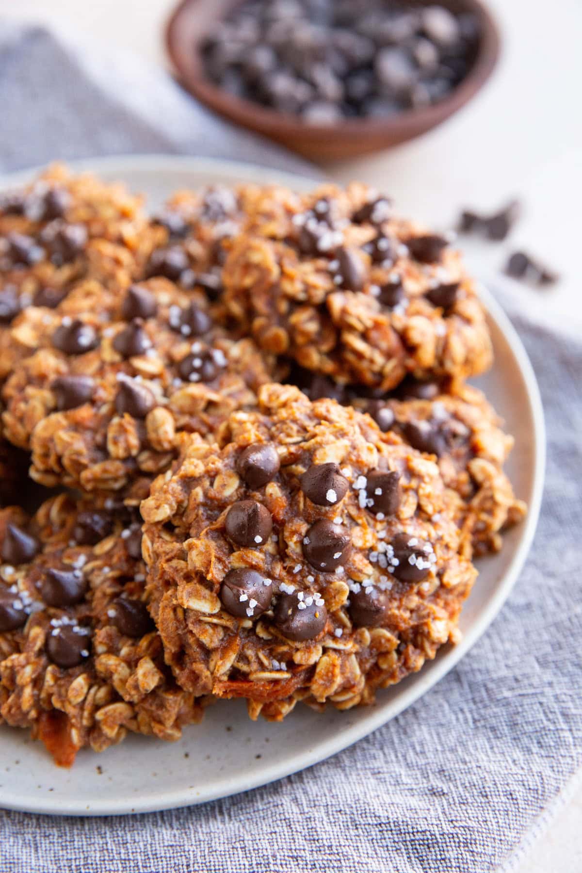 Plate of sweet potato oatmeal cookies with chocolate chips and sea salt. Bowl of chocolate chips in the background.