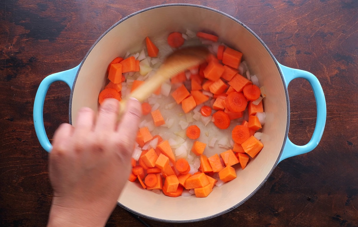 Stirring sweet potatoes, carrots, and onion in a large pot.