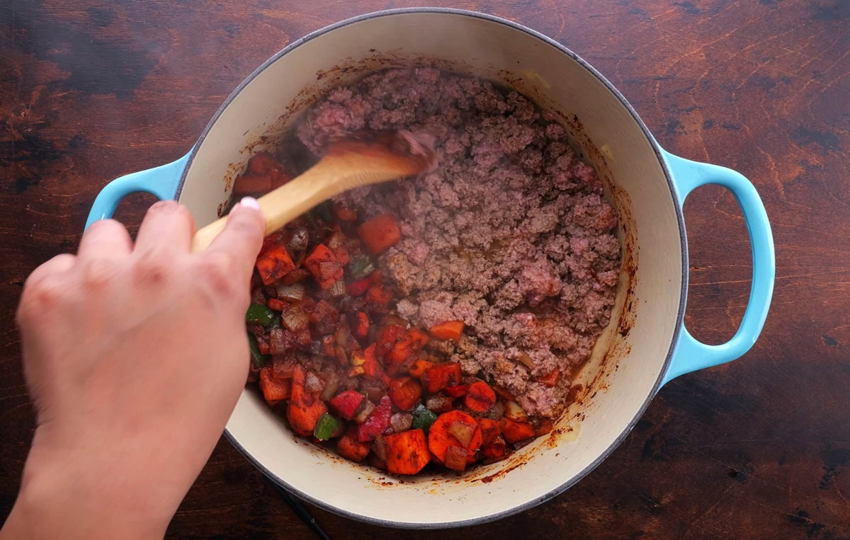 Ground turkey in a large pot with vegetables to the side.