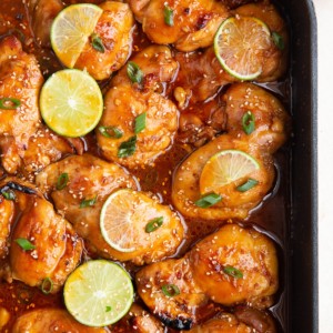 Korean BBQ chicken in a large roasting pan, fresh out of the oven. Sprinkled with green onions and sliced limes on the chicken.